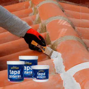 Mano de persona aplicando el sellador Tapa Goteras elastomérico de Megacolor sobre superficie de techo rojo con brocha, junto a cubetas de producto con el logo de Megacolor.