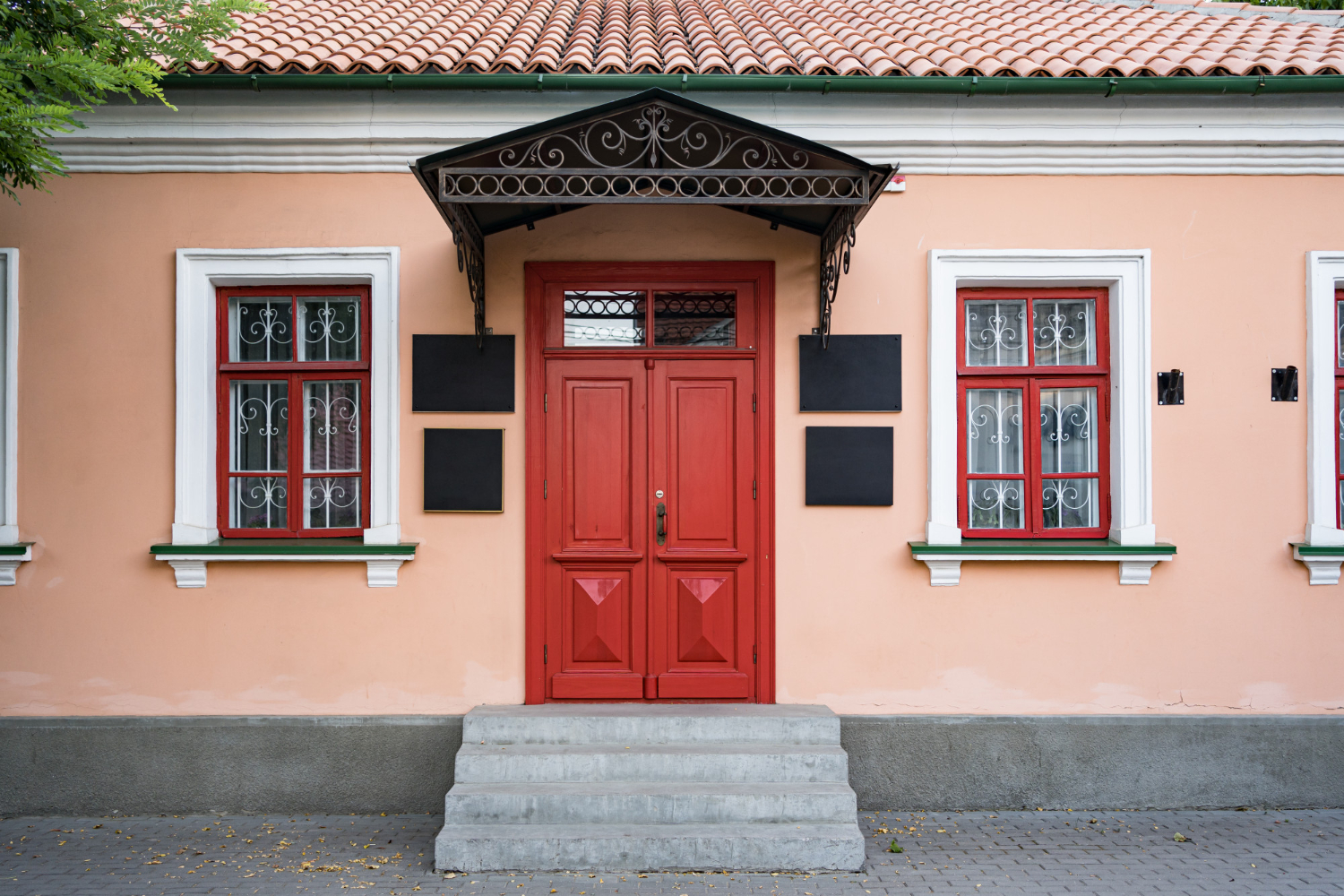 Fachada de una casa histórica con paredes en color melocotón 2024, puerta de entrada roja y ventanas con detalles en hierro forjado, destacando la combinación armoniosa de colores y arquitectura tradicional