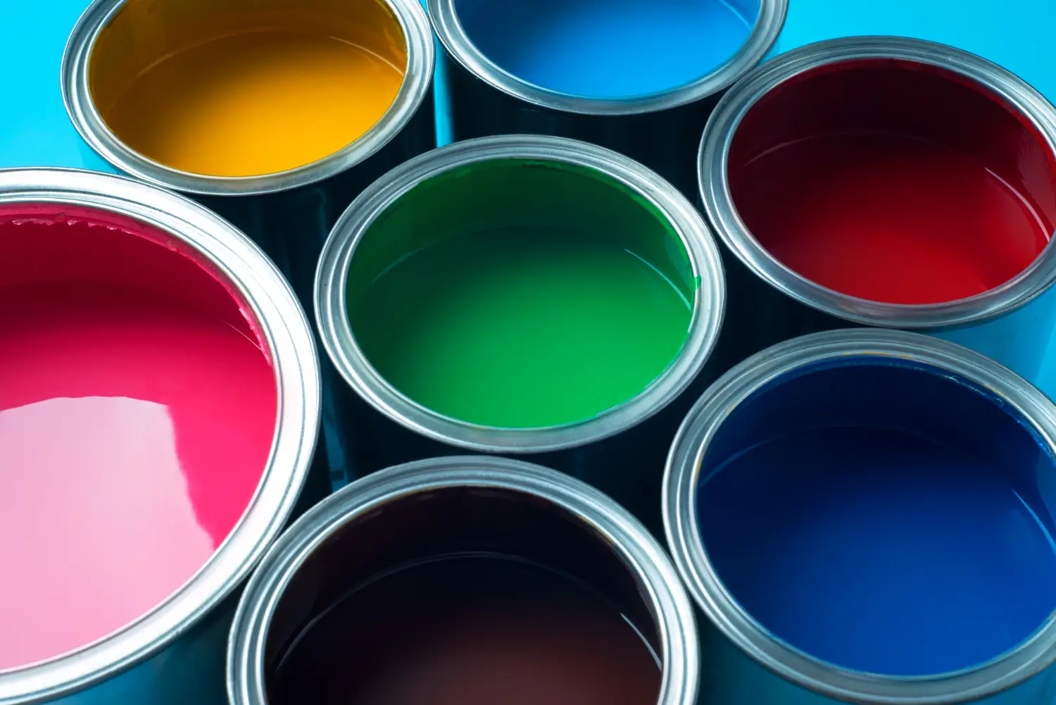 Vista superior de latas abiertas de pintura en una gama vibrante de colores, incluyendo amarillo, rosa, verde, rojo, azul oscuro y azul claro, mostrando la diversidad de opciones de colores de Megacolor.